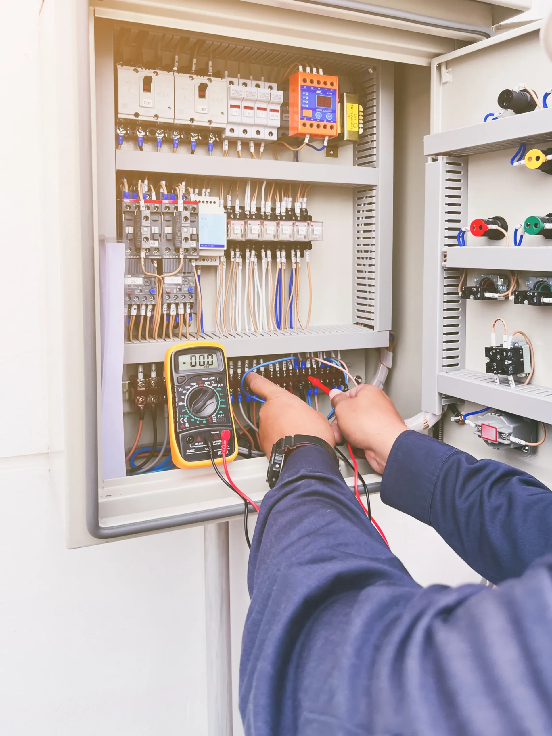 A man working on an electrical panel with a multimeter.